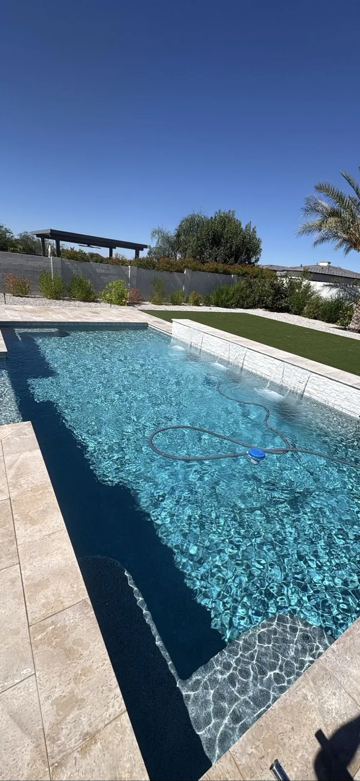 Tiled wall with water scuppers feeding a pool with a vacuum hose in Queen Creek, Arizona