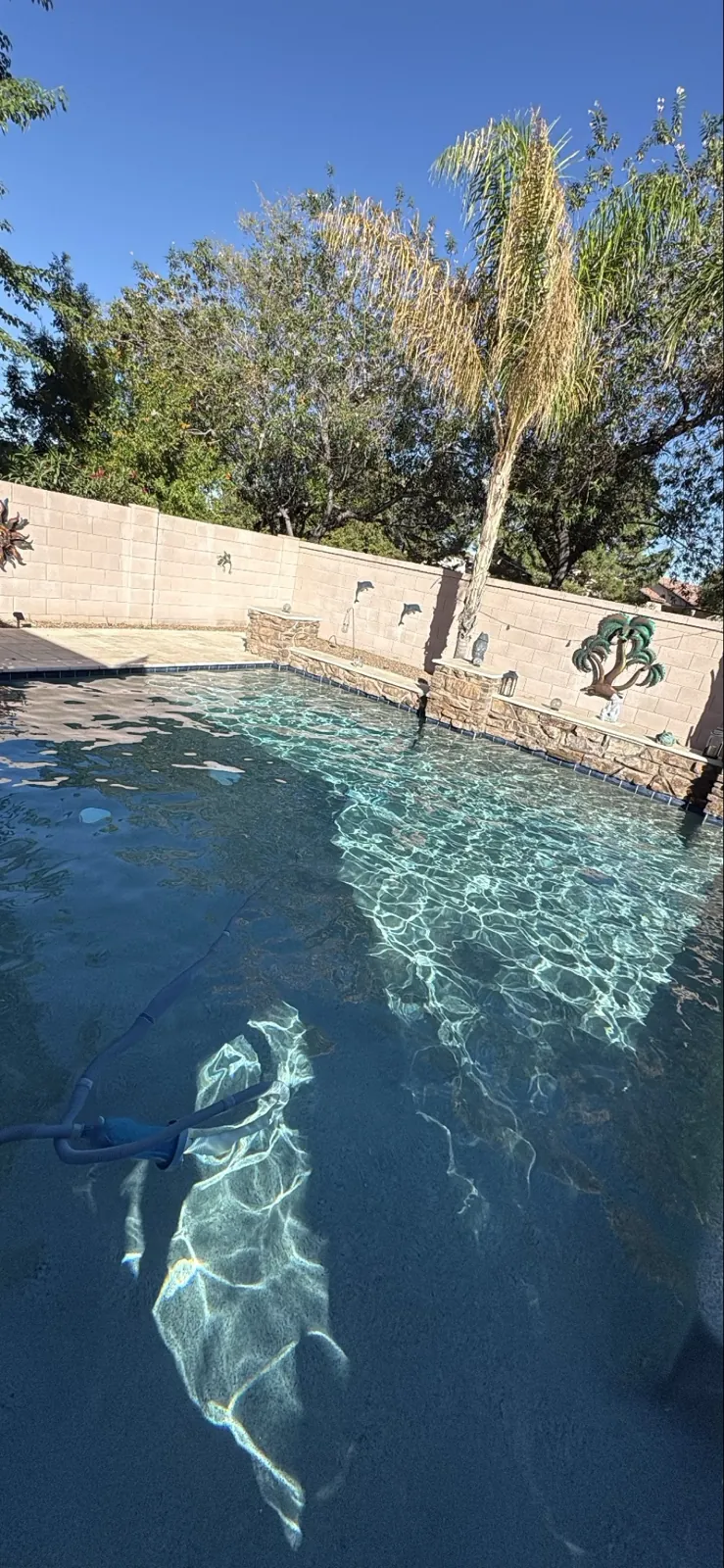 Clear San Tan Valley pool with manual vacuum cleaning the floor near a stone wall feature