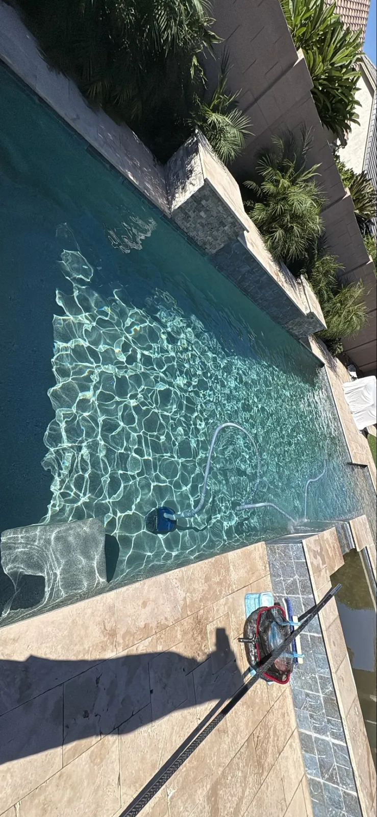 Technician vacuuming a Queen Creek pool with raised stone wall and travertine deck
